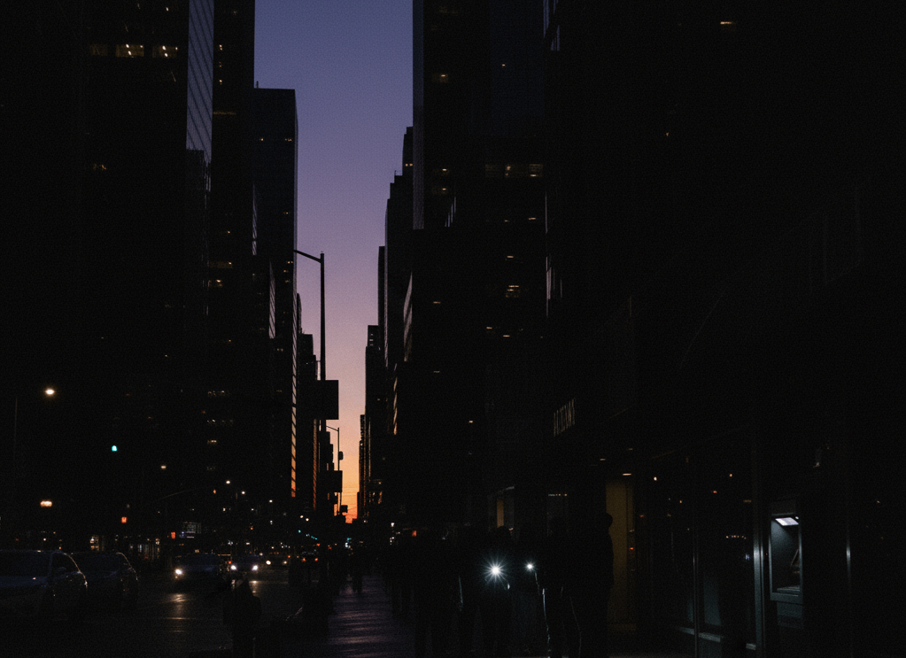 Personas en penumbra en una calle urbana durante un apagón total (sin luces eléctricas). Un cajero automático está inactivo, simbolizando la pérdida de liquidez.